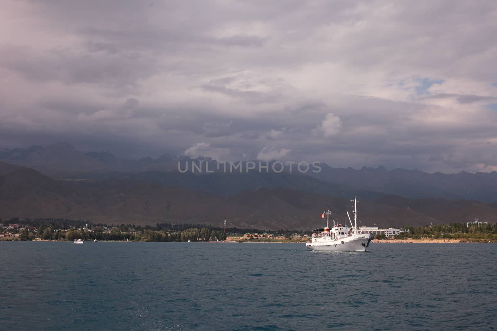 White ship departs from the coast. Mountains of Kyrgyzstan. Blue water in the ocean sea. Beautiful clouds in the sky. by selinsmo