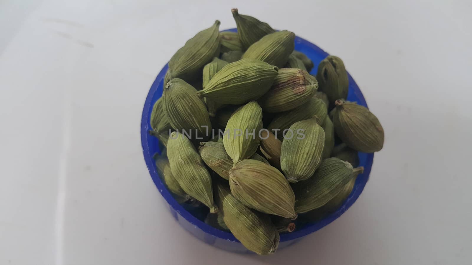 Closeup top view of dried green Elettaria cardamomum fruits with seeds, cardamom spice in small bowl on white background