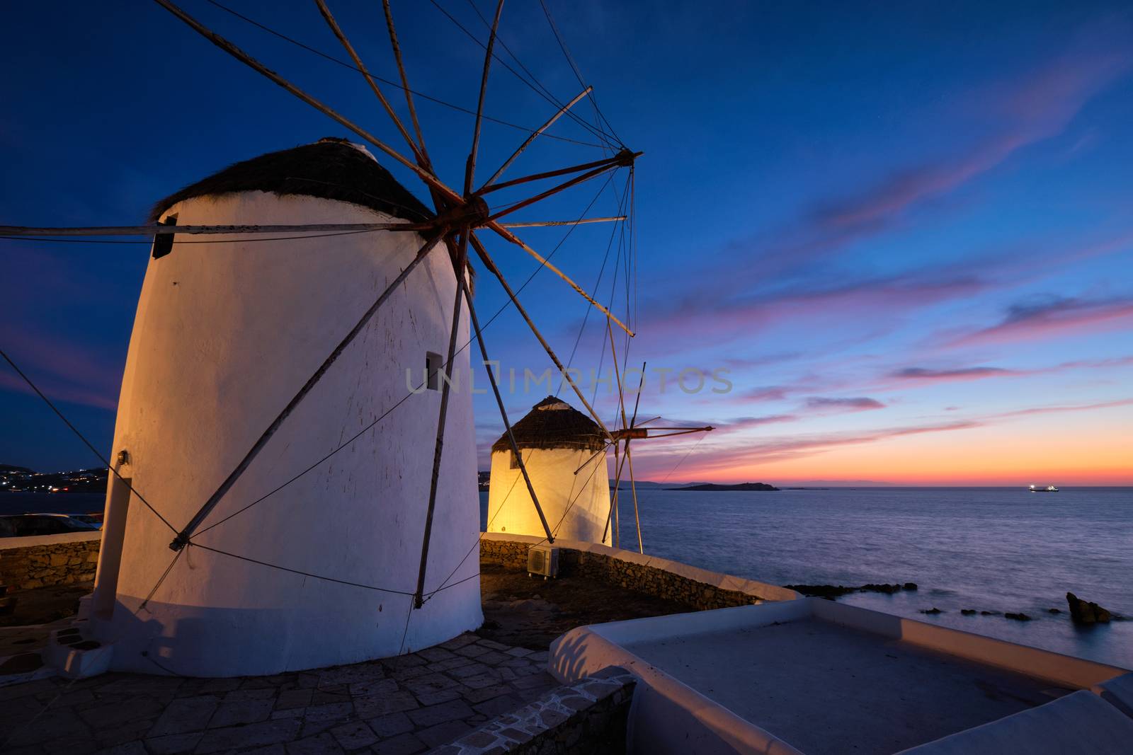 Scenic view of famous Mykonos Chora town windmills. Traditional greek windmills on Mykonos island illuminated in the evening, Cyclades, Greece. Walking with steadycam.