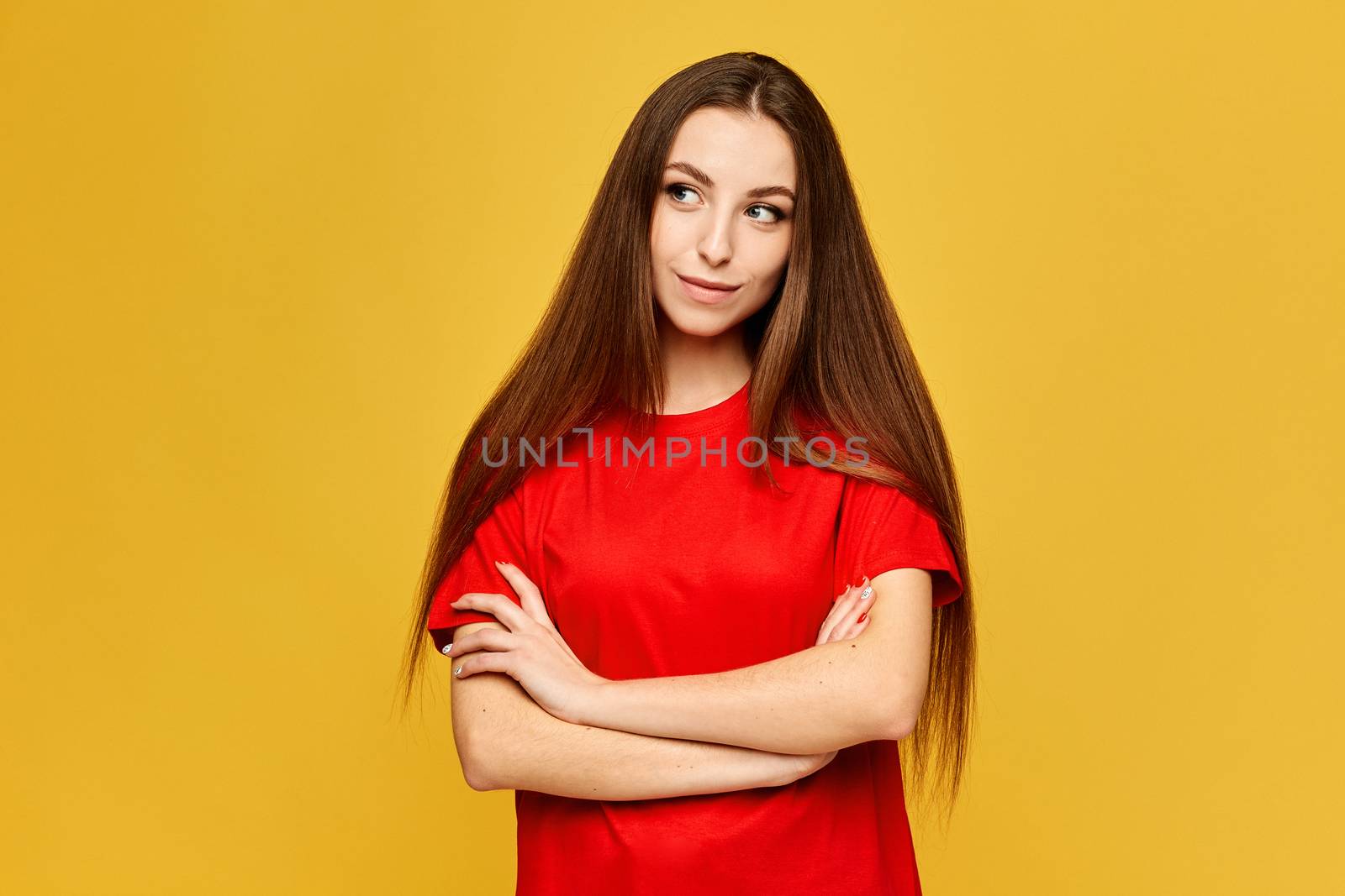Young female student in a red shirt posing with folded hands at the yellow background, isolated.