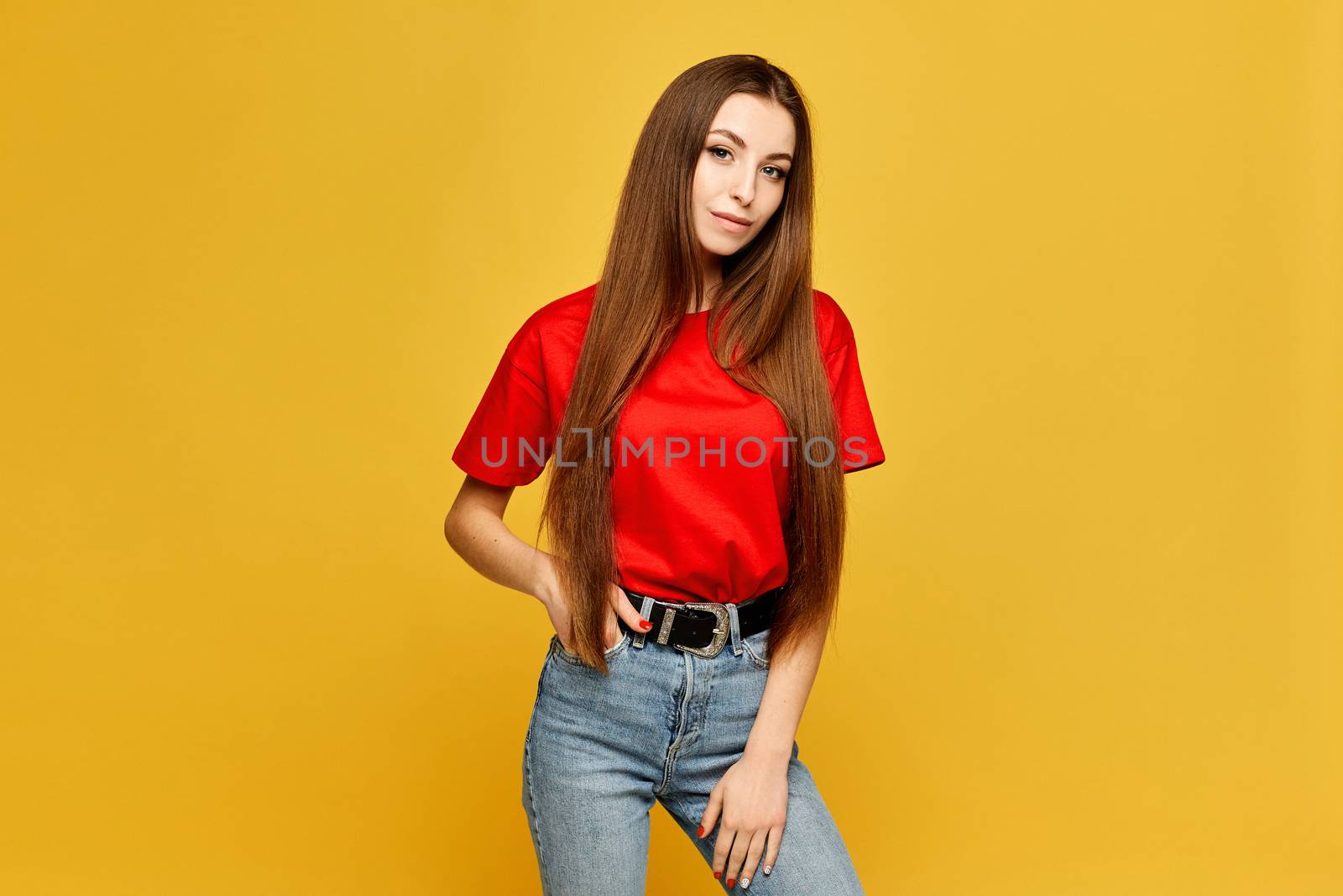 Young woman with slim body in a red blank t-shirt and jeans isolated at the yellow background.