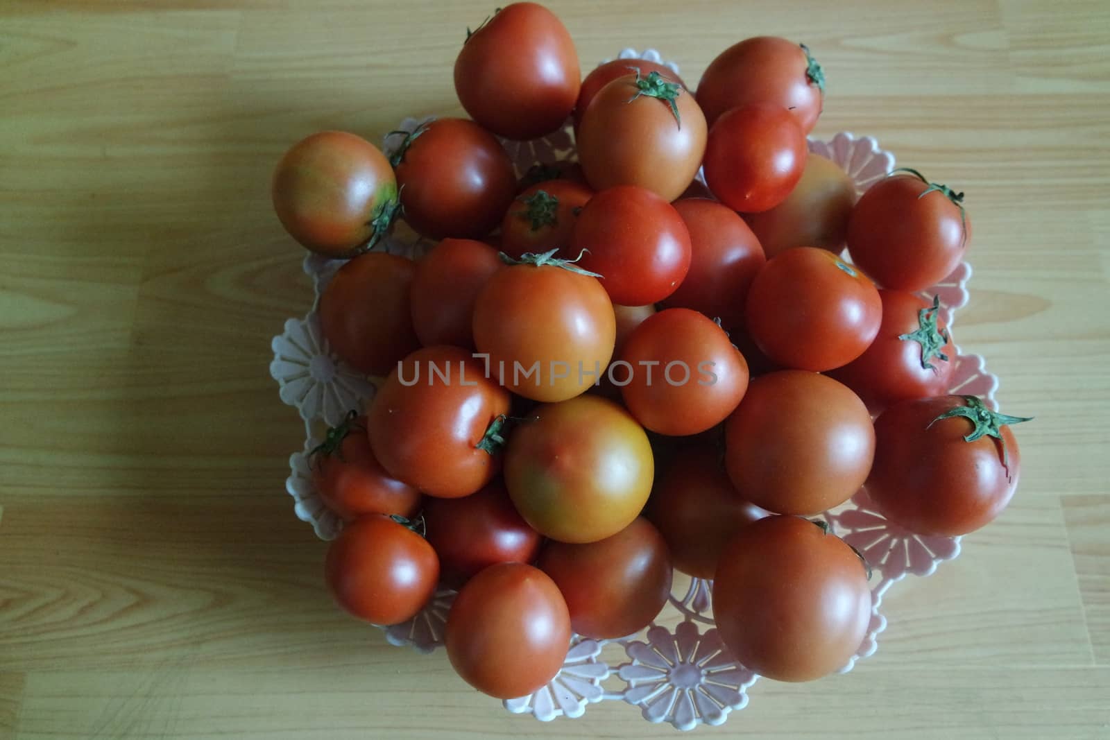 Close-up view of red tomatoes in white basket on a wooden floor in market by Photochowk