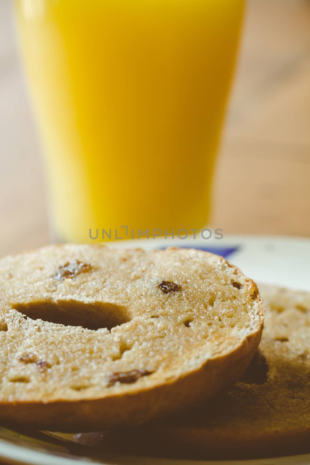 A glass of orange juice and a sliced toasted raisin and cinnamon bagel