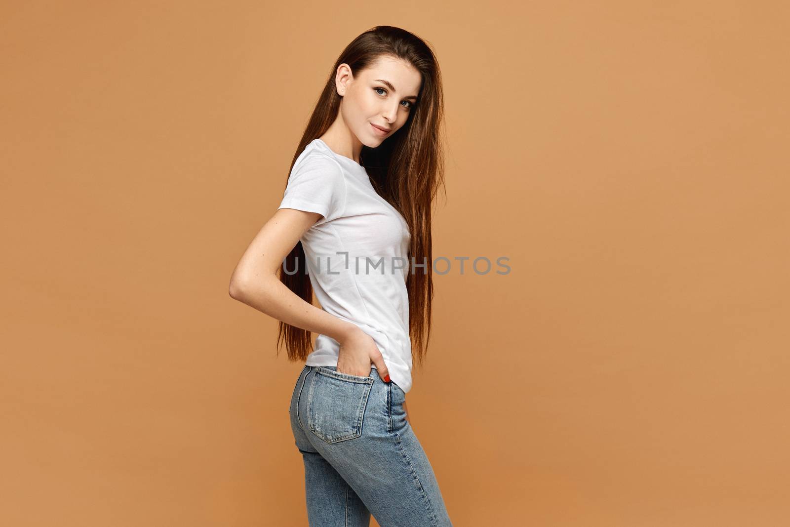 Side view of girl with slim perfect body in a blank white t-shirt at the beige background, isolated. Clothes advertisement mockup.
