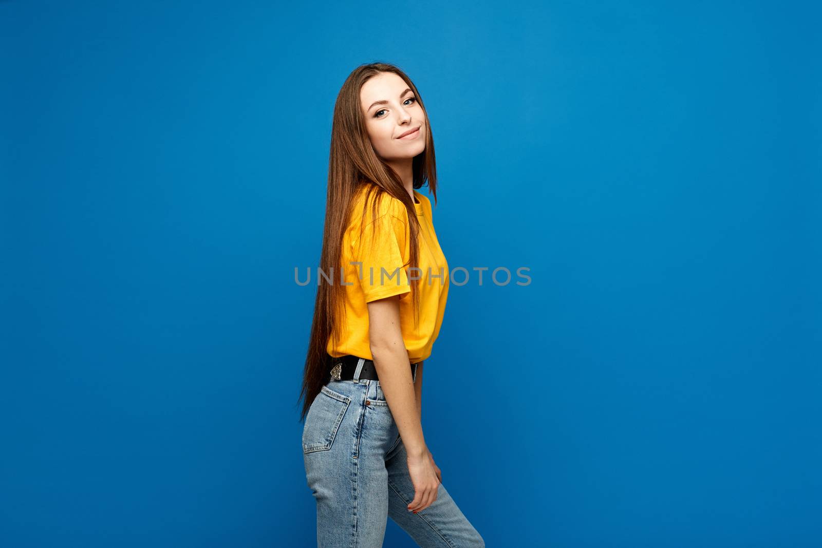 Side view of a model girl with slim body in oversized yellow t-shirt and jeans at the blue background, isolated.