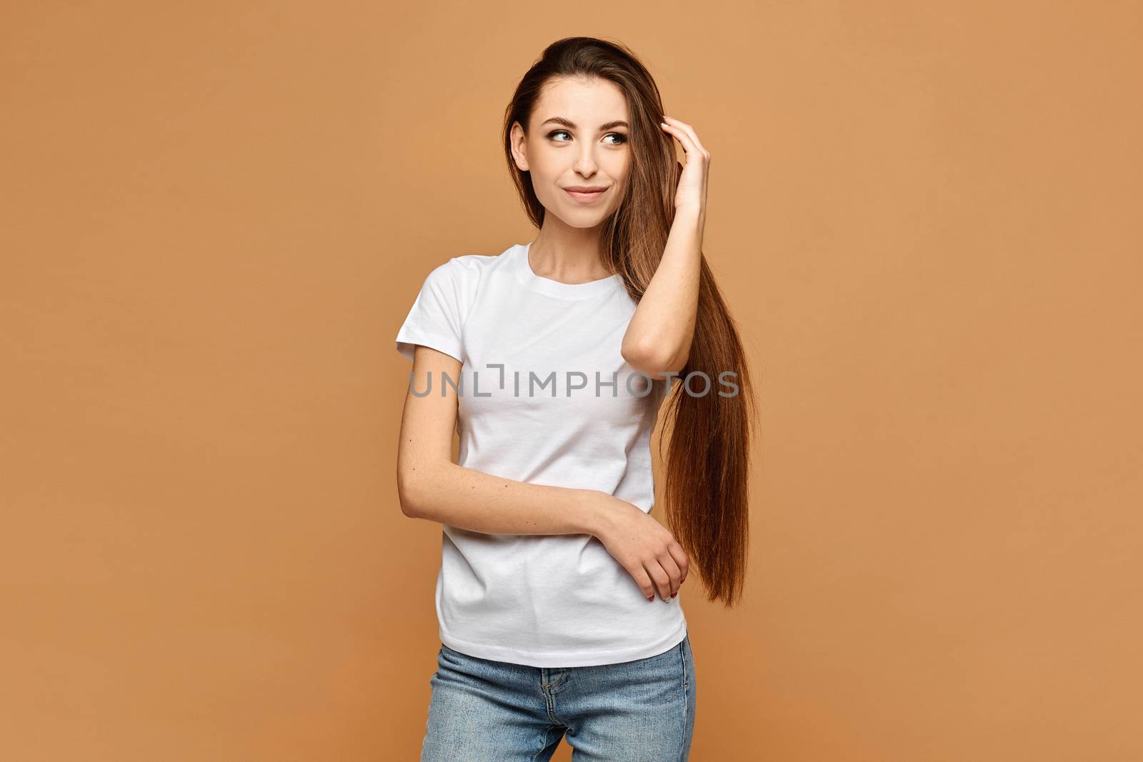 A young woman in white shirt and blue jeans at beige background, isolated. Model girl in a casual outfit. Mock-up.