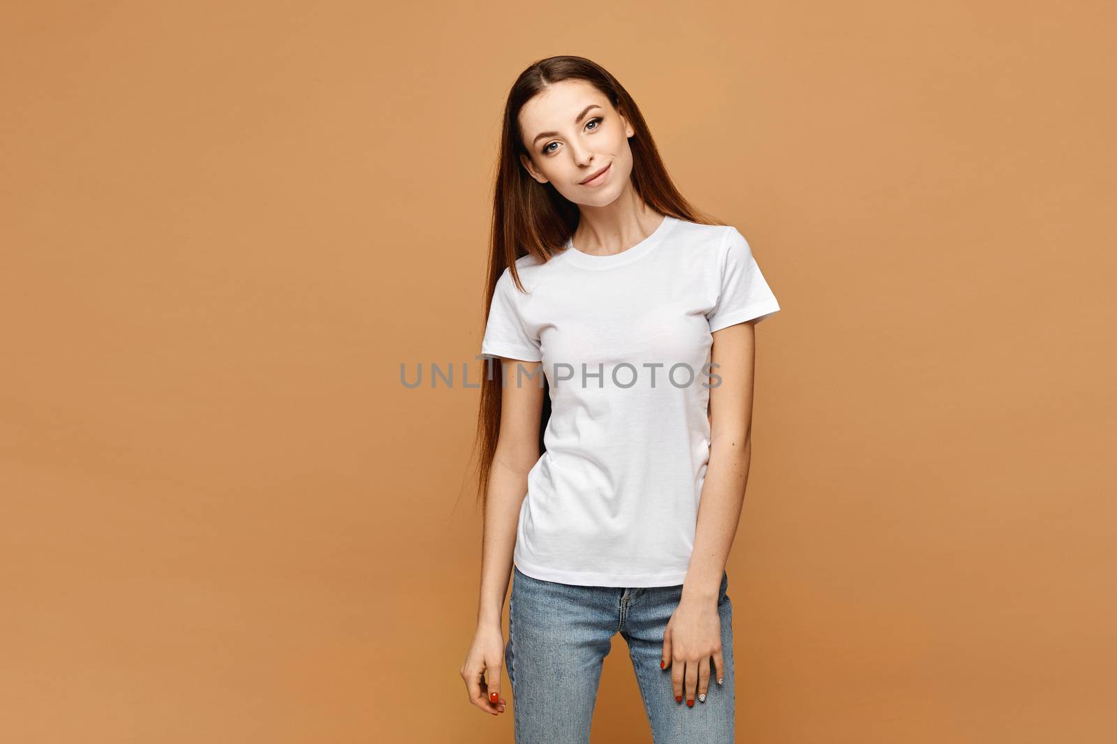 Young woman in white blank t-shirt and blue jeans isolated at beige background, studio close-up. Model girl in a casual outfit. Isolated with copy space.