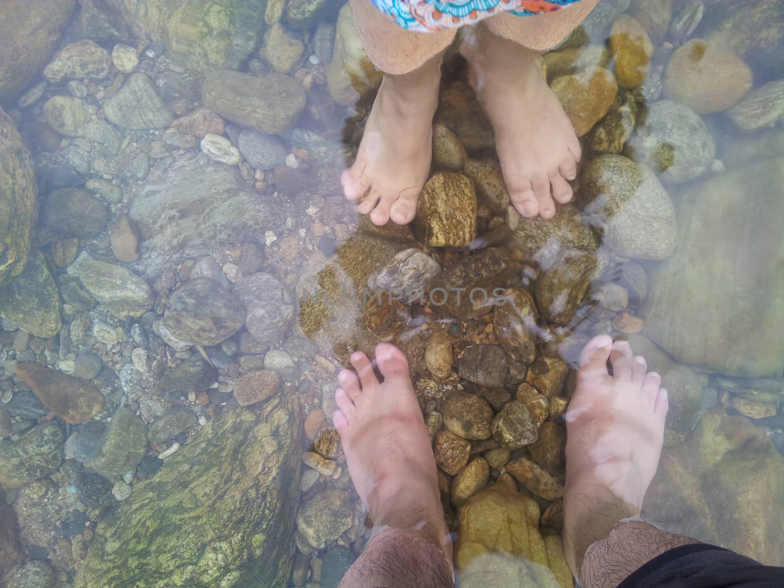 Top view of transparent water surface with human feet visible in it. Copy space for background and texture. Transparent water texture with view of stones under water.