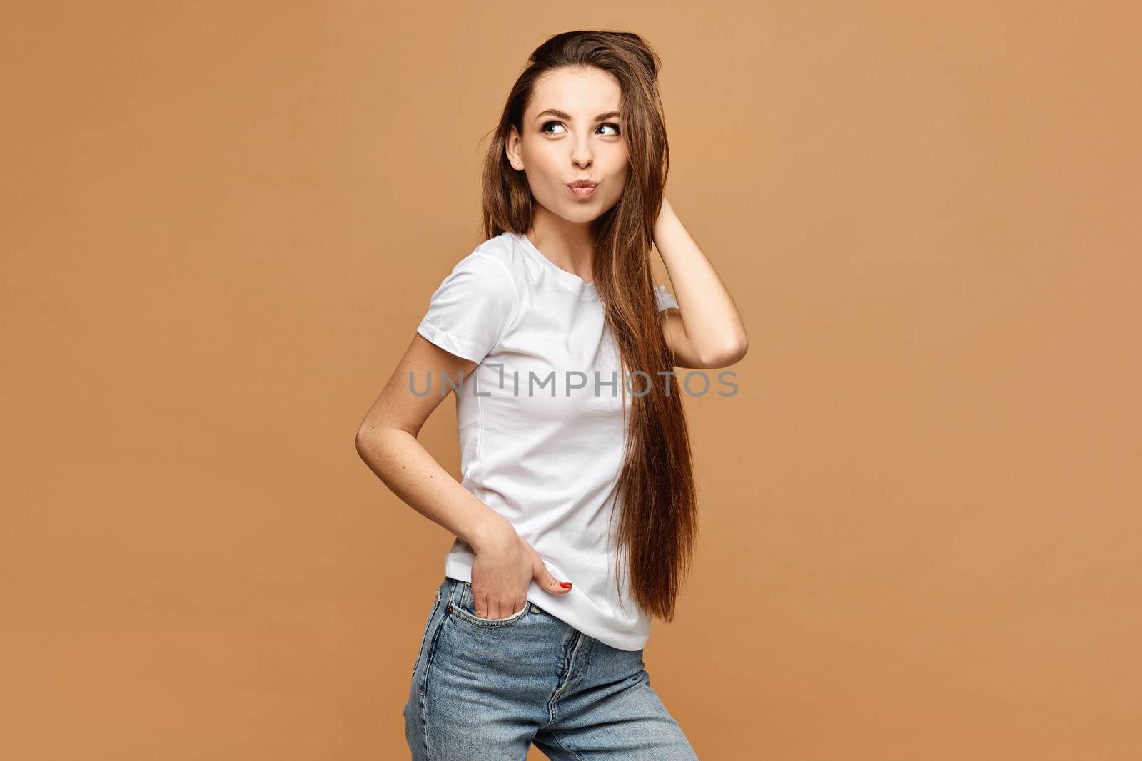 Model girl with slim body in a white t-shirt posing with one hand in pocket at the beige background, isolated. Clothes advertisement mock-up.