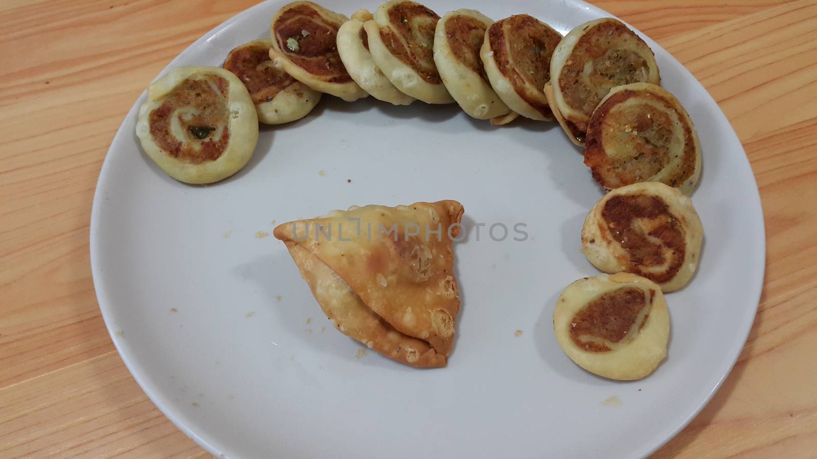 Closeup of delicious home made pinwheel puff and samosa pastries food item placed in a white ceramic plate on wooden floor