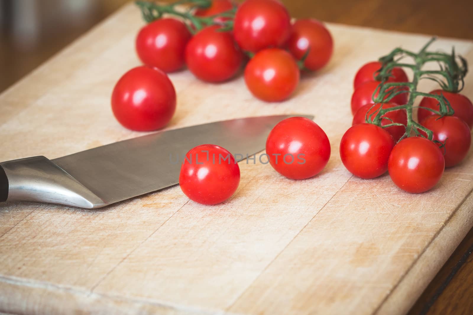Cherry tomatoes (Solanum lycopersicum) and a knife on a wooden chopping board