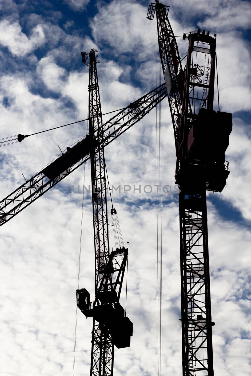 Three tower cranes silhouetted against a cloud filled sky