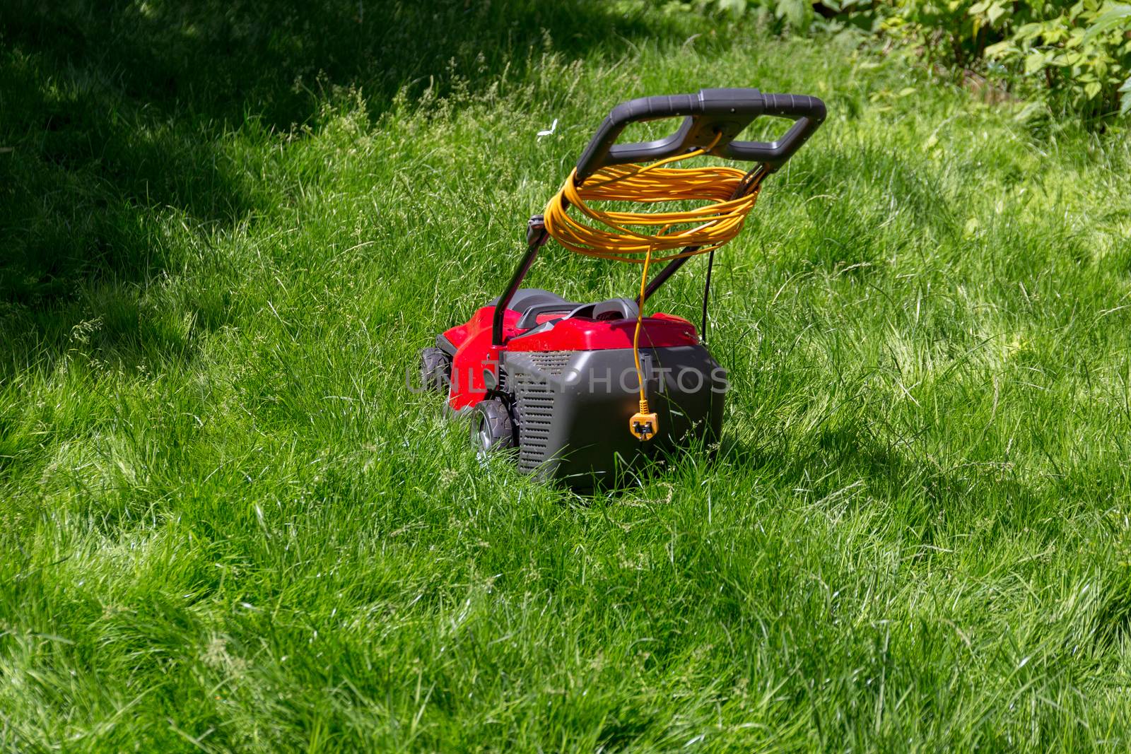 A lawnmower on a lawn of long grass in need of cutting