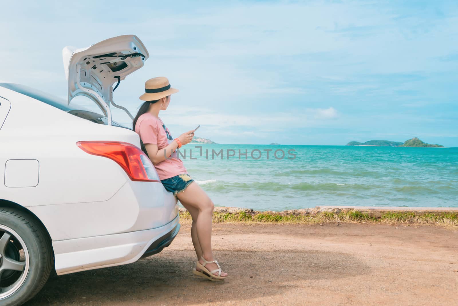 Women hold a smartphone sitting with a beach car
