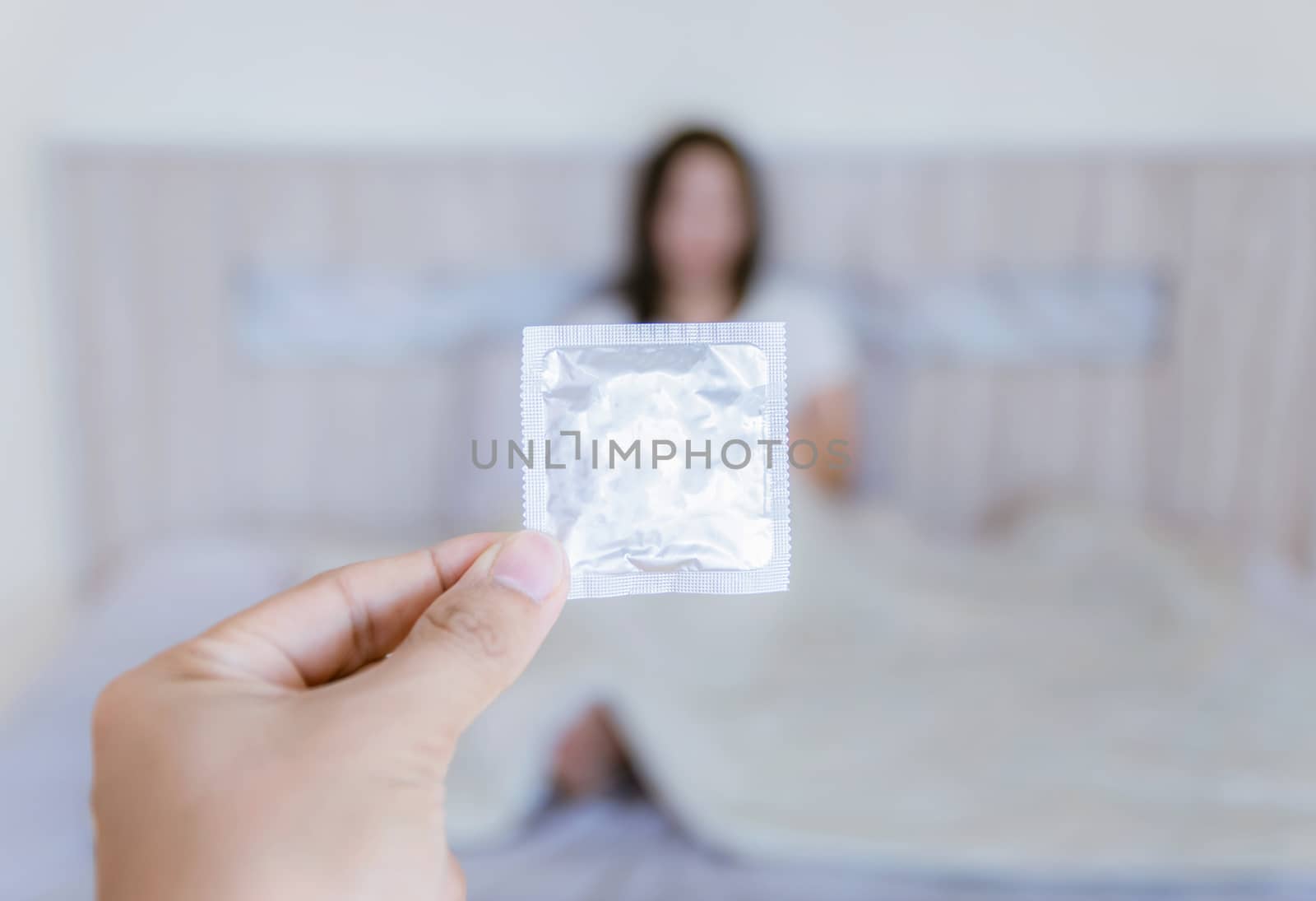 The man with the hand a condoms of the woman lying on the bed is blurred