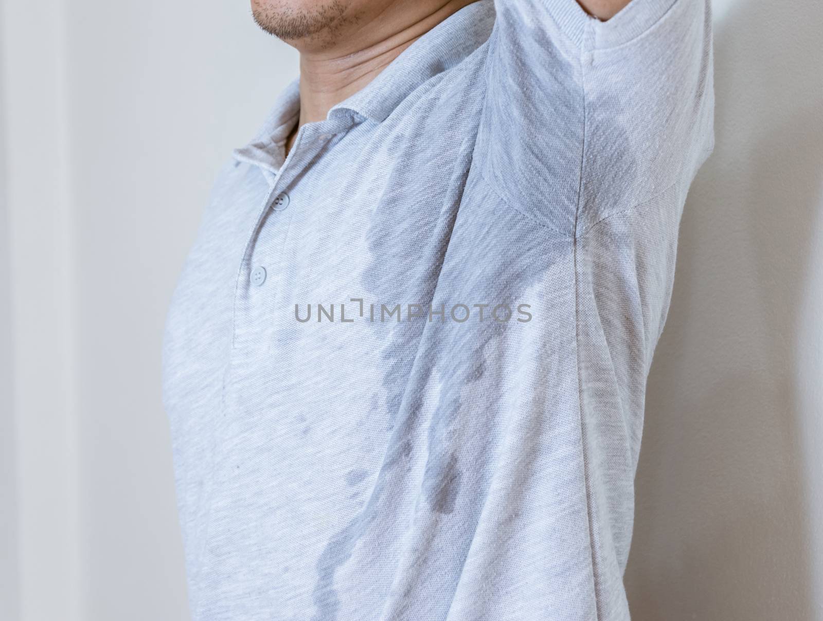 Man with sweat stain on clothes against, using deodorant