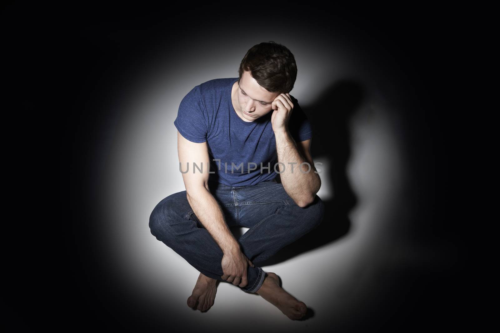 Unhappy Young Man Sitting In Pool Of Light