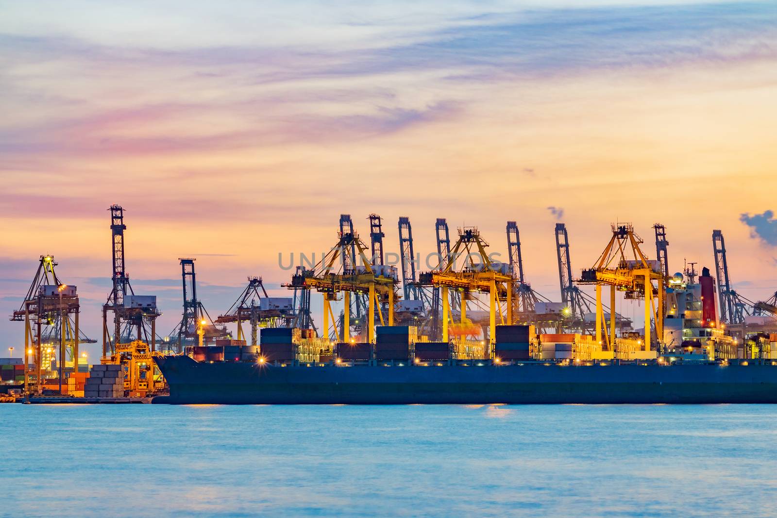 Freighter ship loading cargo at loading dock on twilight time. Singapore, south east asia.