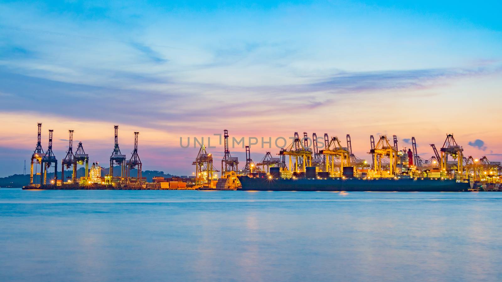 Freighter ship loading cargo at loading dock on twilight time. Singapore, south east asia.