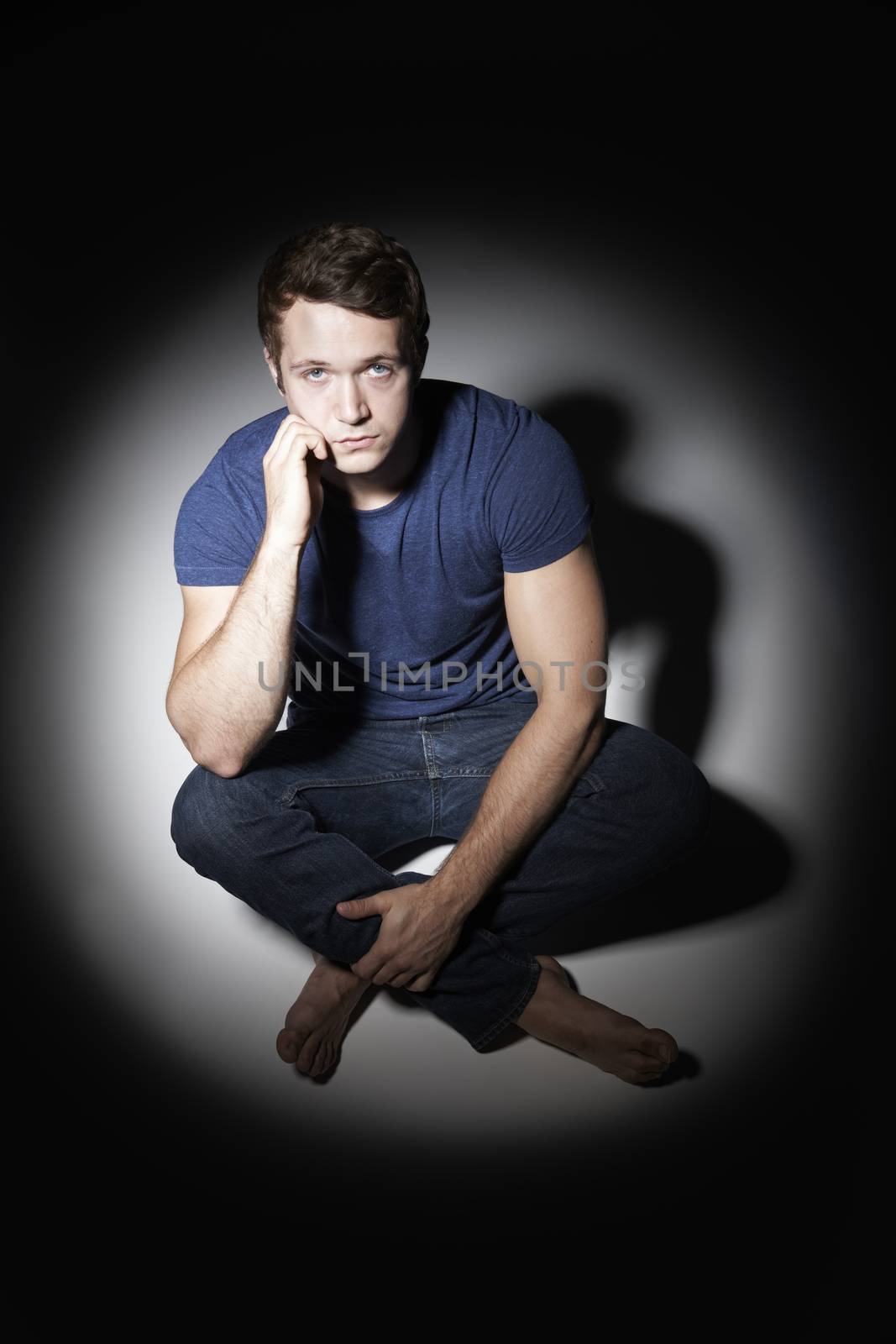 Portrait Of Unhappy Young Man Sitting In Pool Of Light