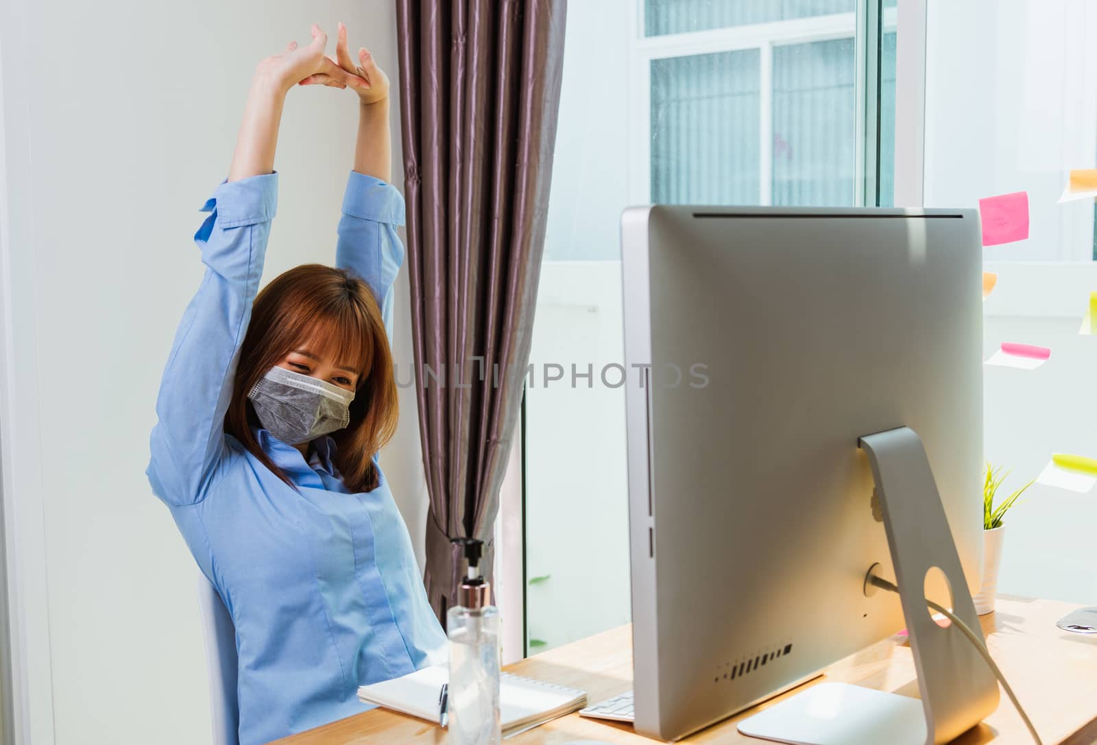 Work from home concept, Happy Asian beautiful young business woman wearing face mask protective quarantines disease coronavirus or COVID-19 her stretching her arms above her head after success work