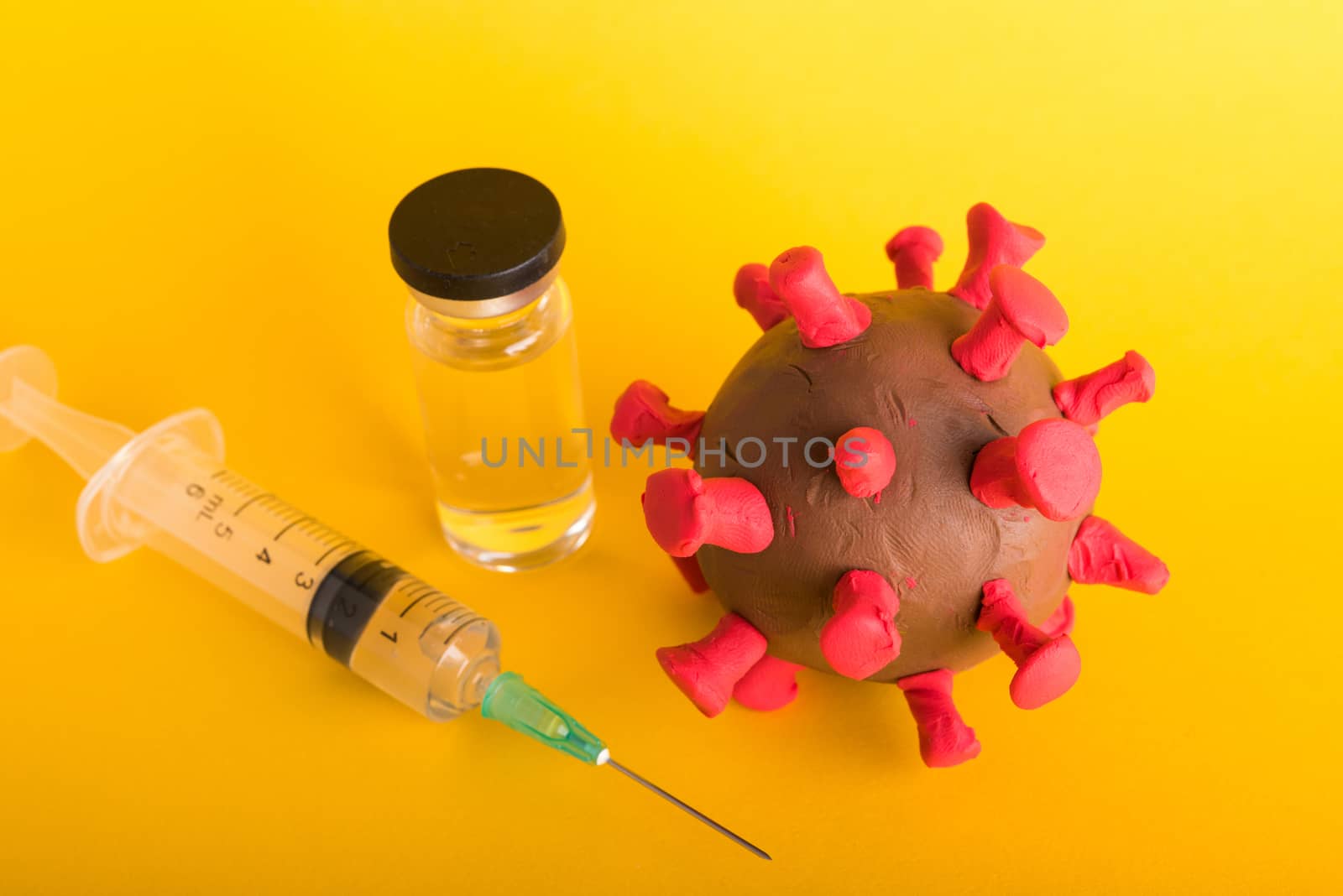 Closeup plasticine disease cells virus bottle vaccine and syringe of coronavirus outbreak and coronaviruses influenza flu, studio shot isolated on yellow background, pandemic COVID-19 medical health