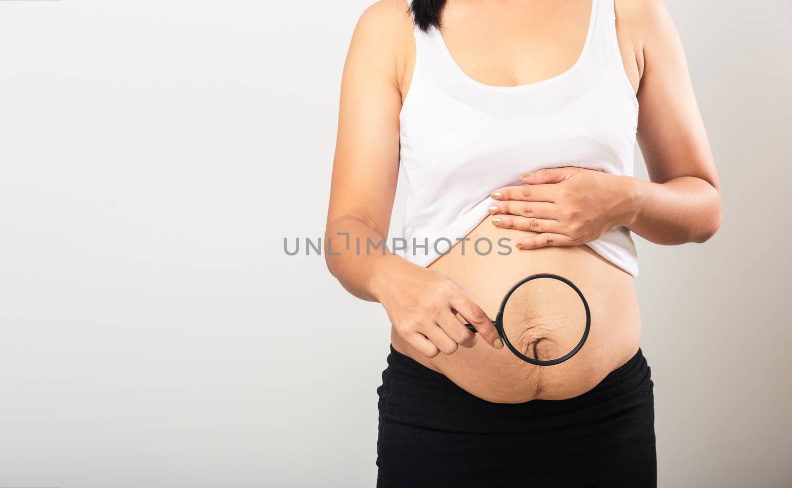 Close up of Asian mother woman use magnifying glass show stretch mark loose lower abdomen skin she fat after pregnancy baby birth isolated on white background, Healthy belly excess body concept