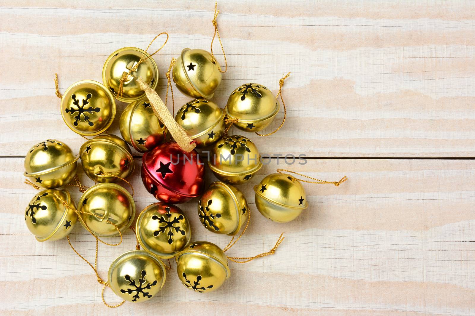 High angle shot of a group of Christmas jingle bells on a white wood table. Horizontal format  with one red bell surrounded by a lot of smaller gold bells.