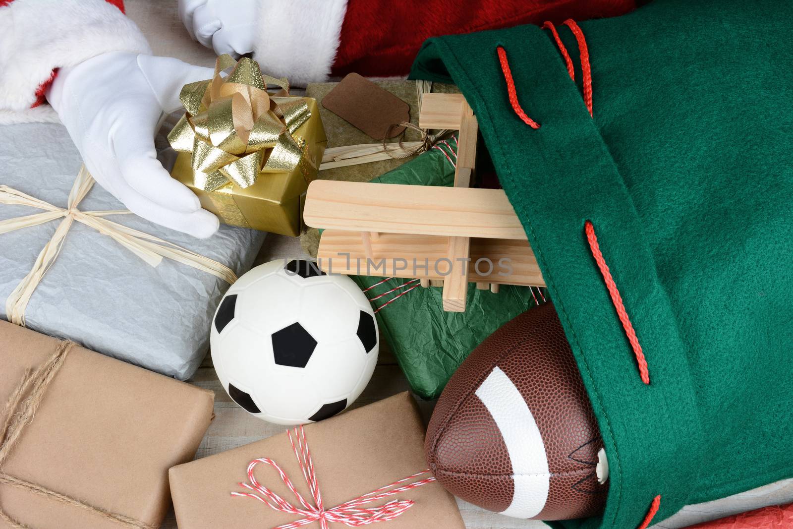 Closeup of Santa Claus filling his bag with toys and presents. Only Santa's hands are visible. Wrapped presents soccer ball, football, toy airplane and gifts fill the frame. Horizontal format.