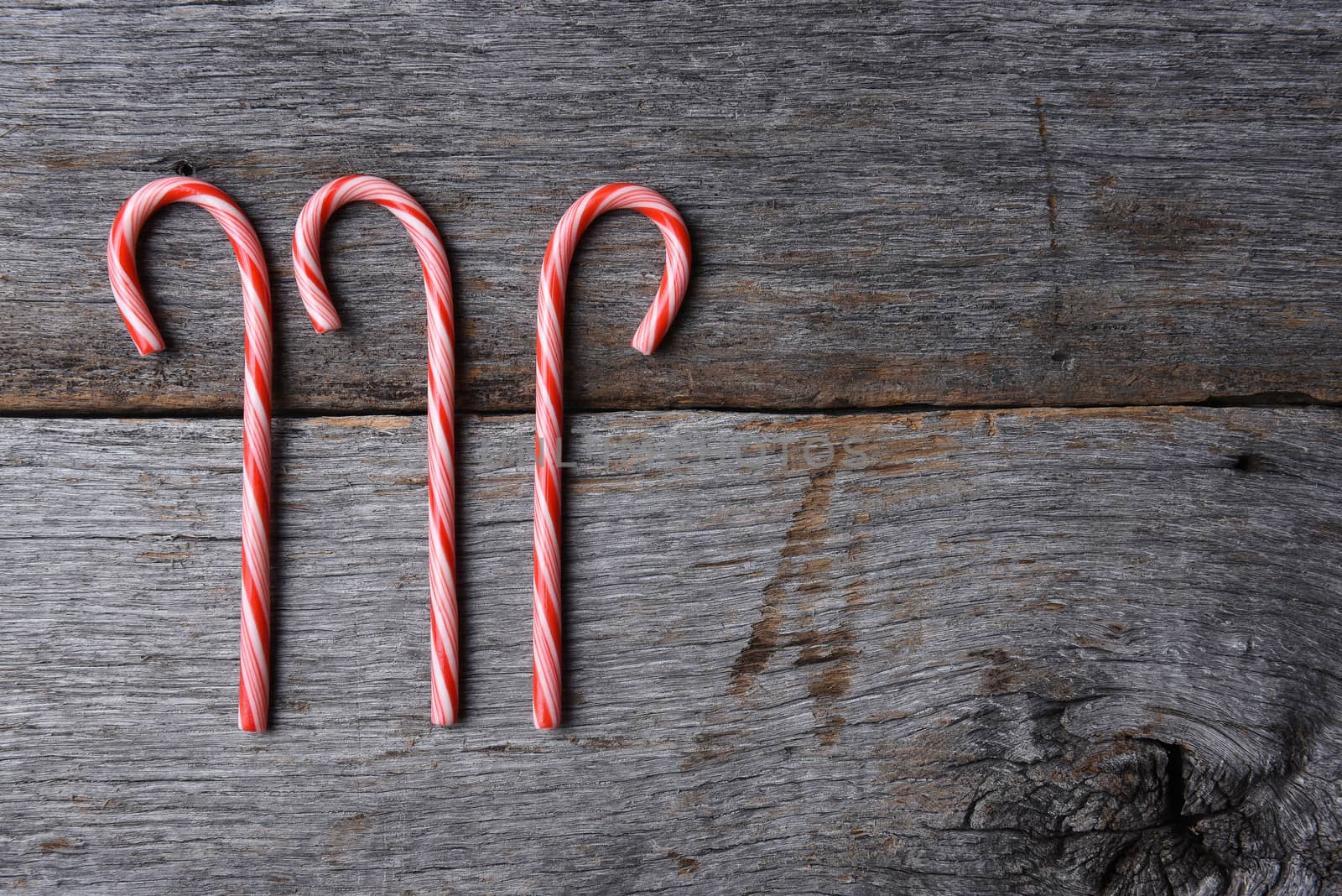 High angle shot of three holiday candy canes on a rustic wood table. Horizontal format with copy space.