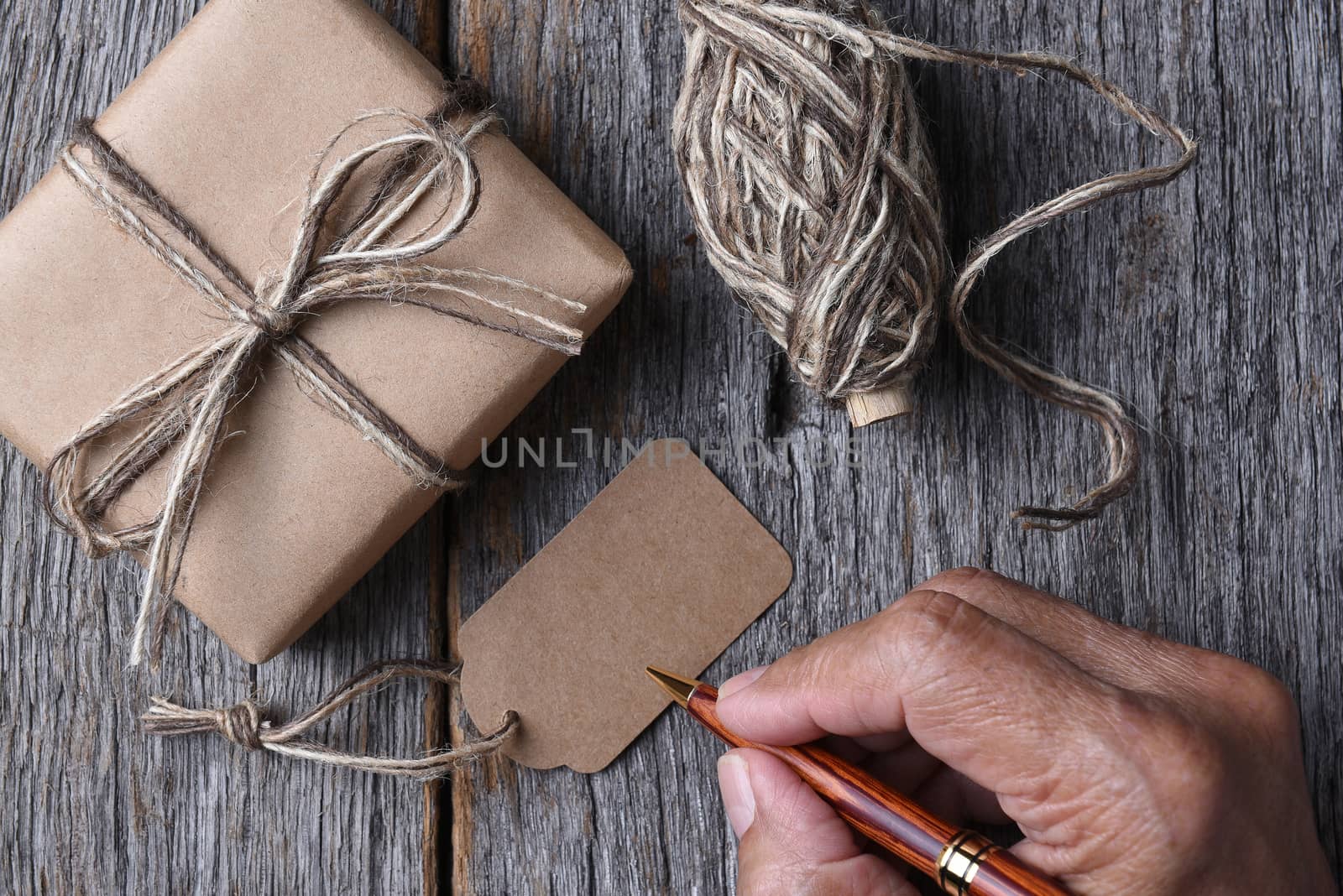 Closeup of a plain wrapped Christmas gift with a man ready to fill out the blank tag. 