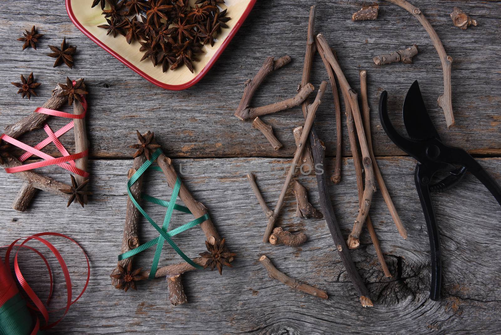 Top view of the equipment and supplies for making rustic Christmas decorations, including twigs, star anise, shears, and ribbon.