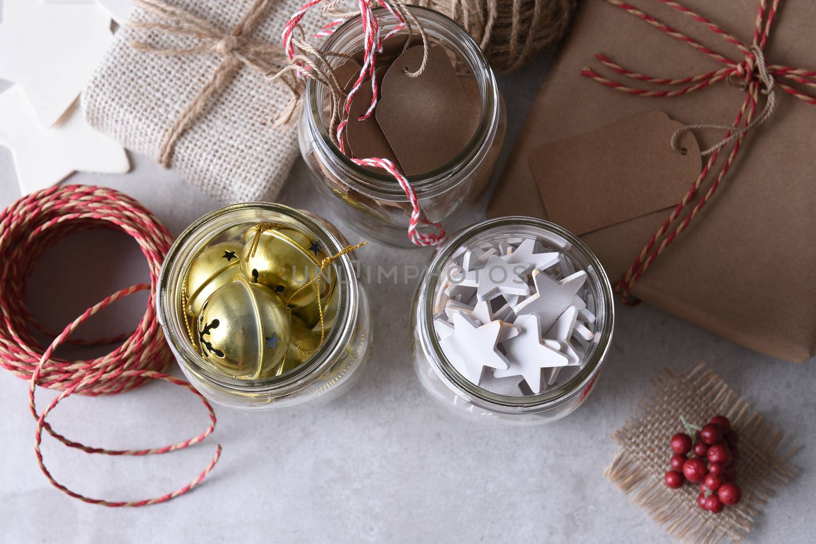 Christmas present wrapping supplies. High angle shot of three mason jars with gift tags, wood stars, and sleigh bells agains a rustic white wood wall.