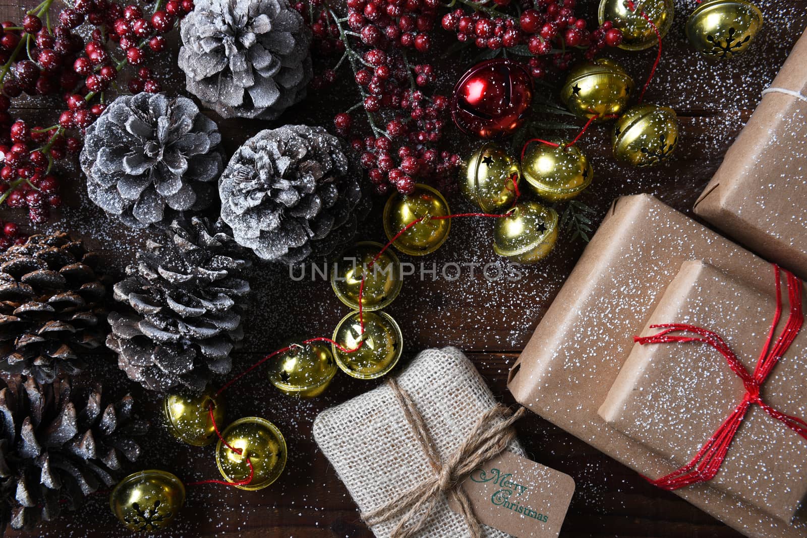 Wrapped christmas presents, Jingle bells, pine cones and red berries on a rustic wood table with snow. 