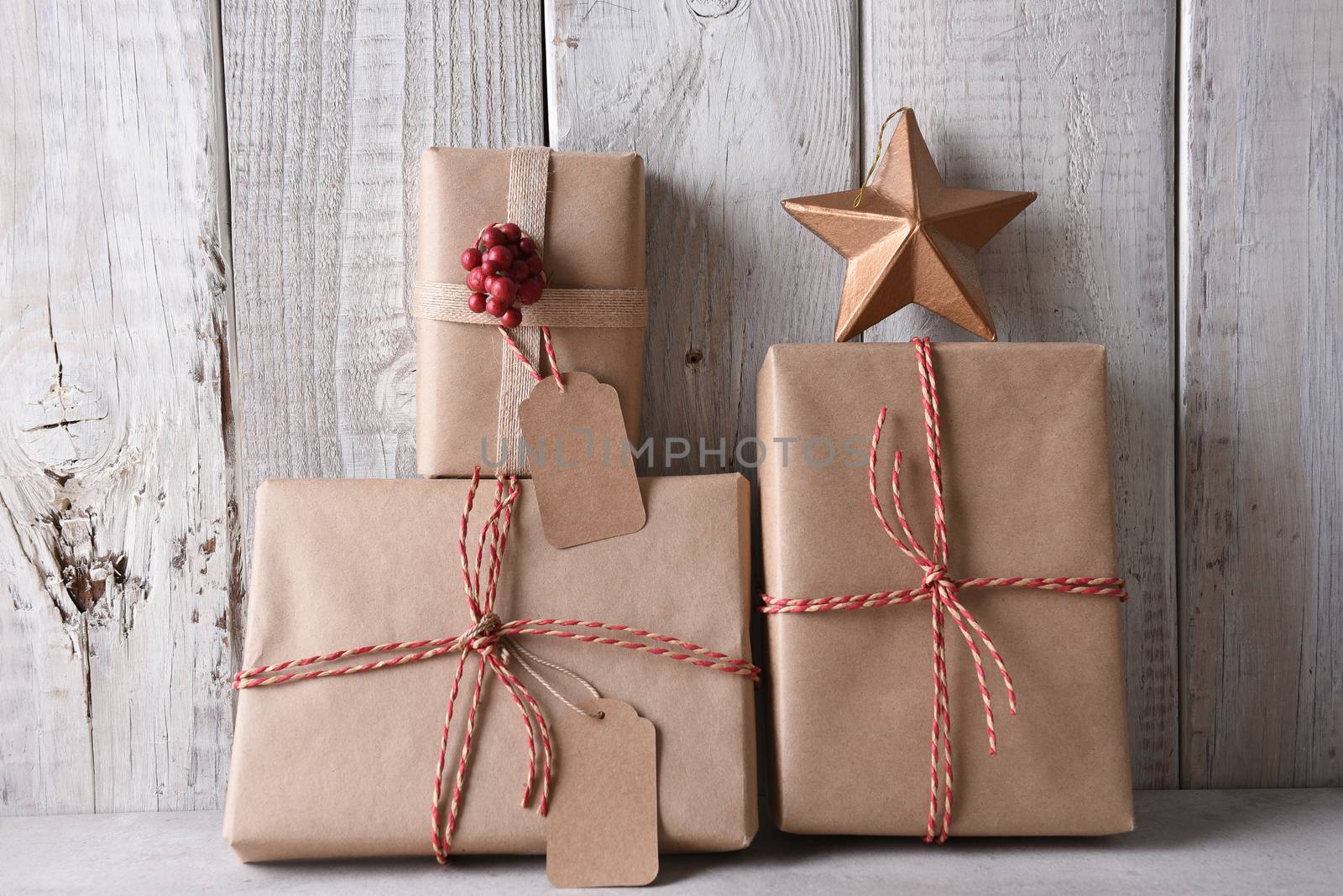 Plain brown paper wrapped Christmas presents. The presents are leanng on a rustic whitewashed wall.