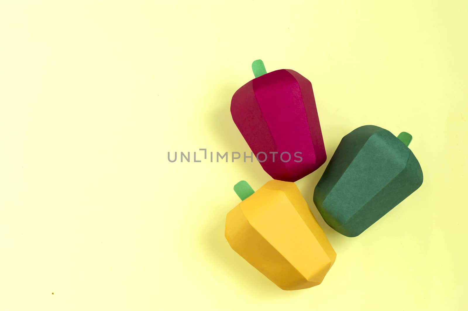 Three multicolored paper peppers on yellow background. Real volumetric handmade paper objects. Paper art and craft