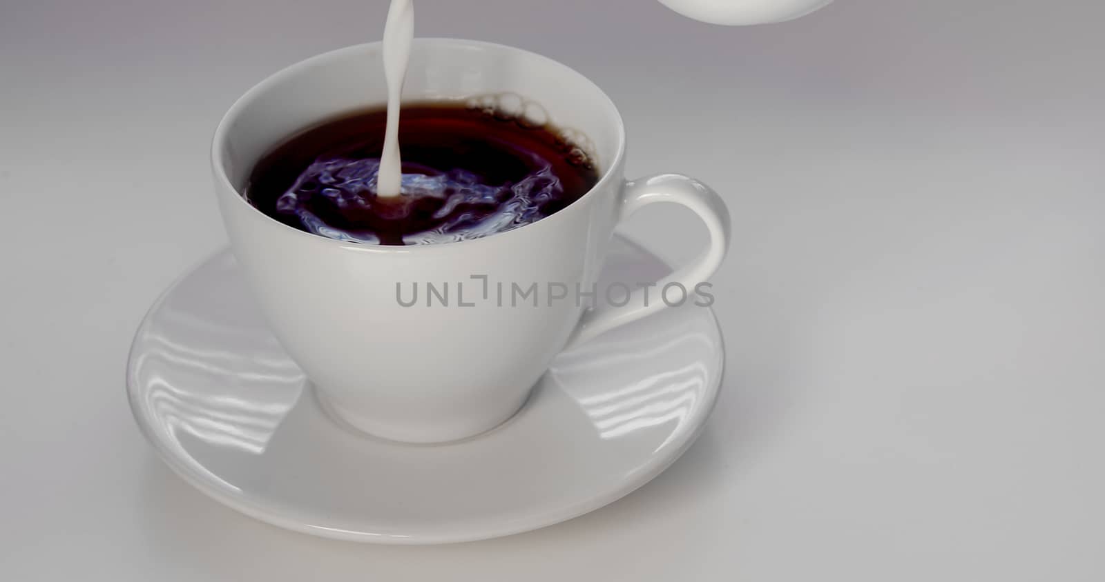 Pouring cream on an cup of coffee on a white background by oasisamuel