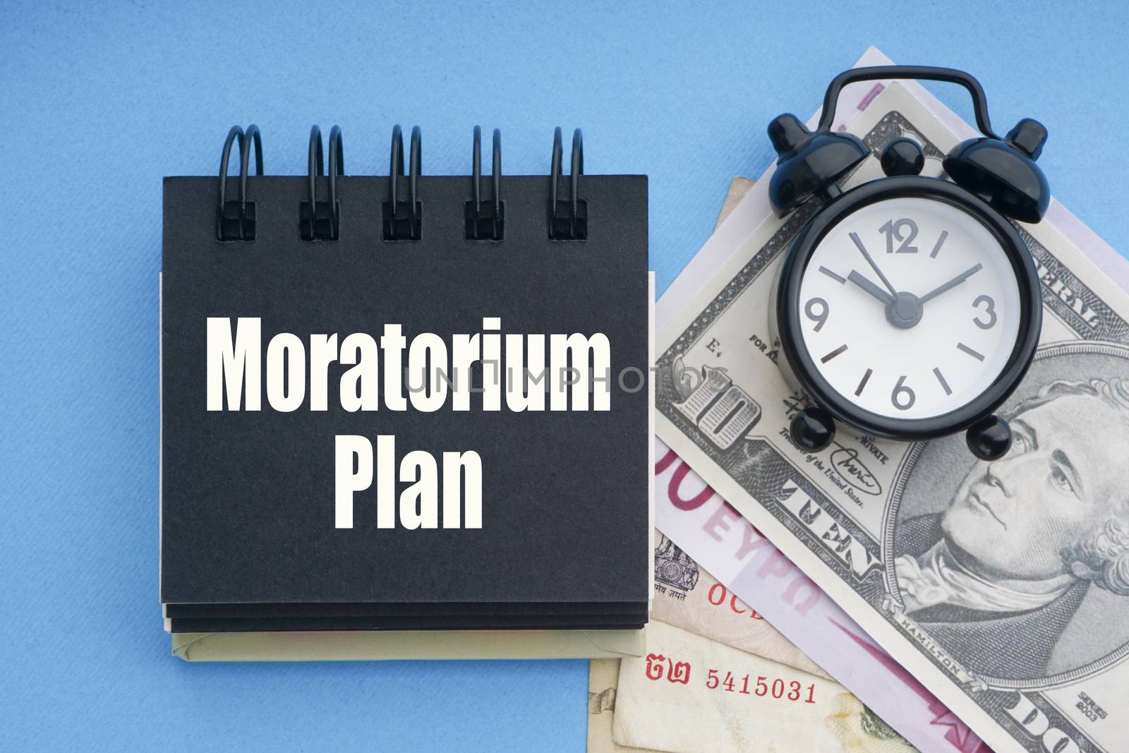 MORATORIUM PLAN text with alarm clock, banknotes currencies on blue background by silverwings