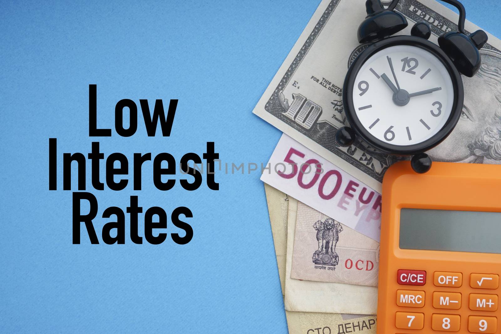 LOW INTEREST RATES text with alarm clock, banknotes currencies and calculator on blue background by silverwings