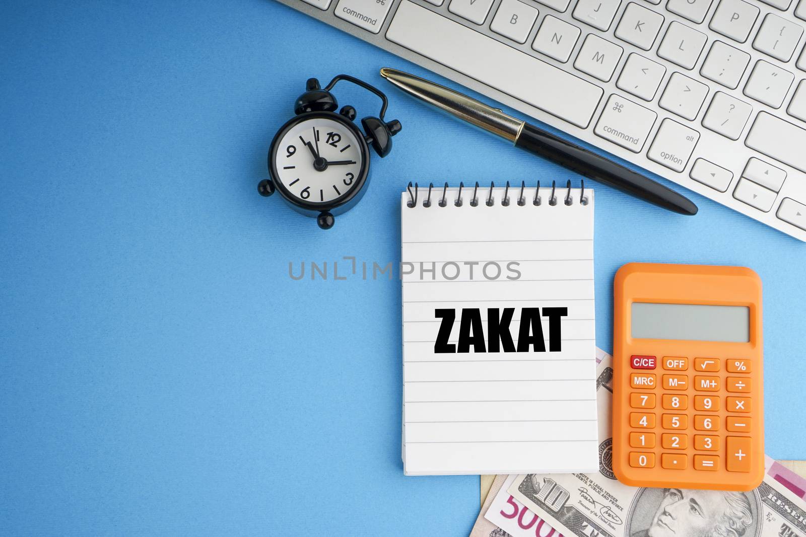 ZAKAT or Islamic Tax on wealth text with fountain pen, notepad, banknotes currency and keyboard on blue background by silverwings