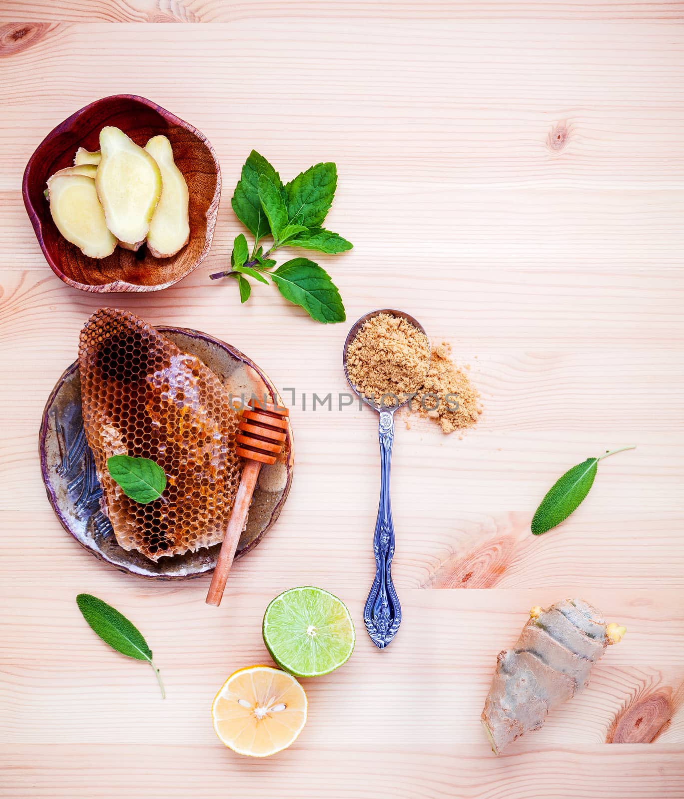 Ingredients for a healthy ginger tea honeycomb in wooden bowl with  pepper mint ginger root and sage leaves set up on white wooden background. Flat lay.