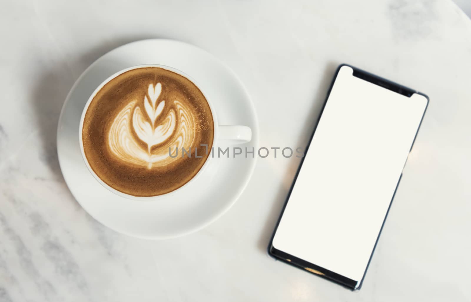 mobile phone blank screen with Cappuccino coffee on marble table in coffee shop. mockup advertising. by barameeyay