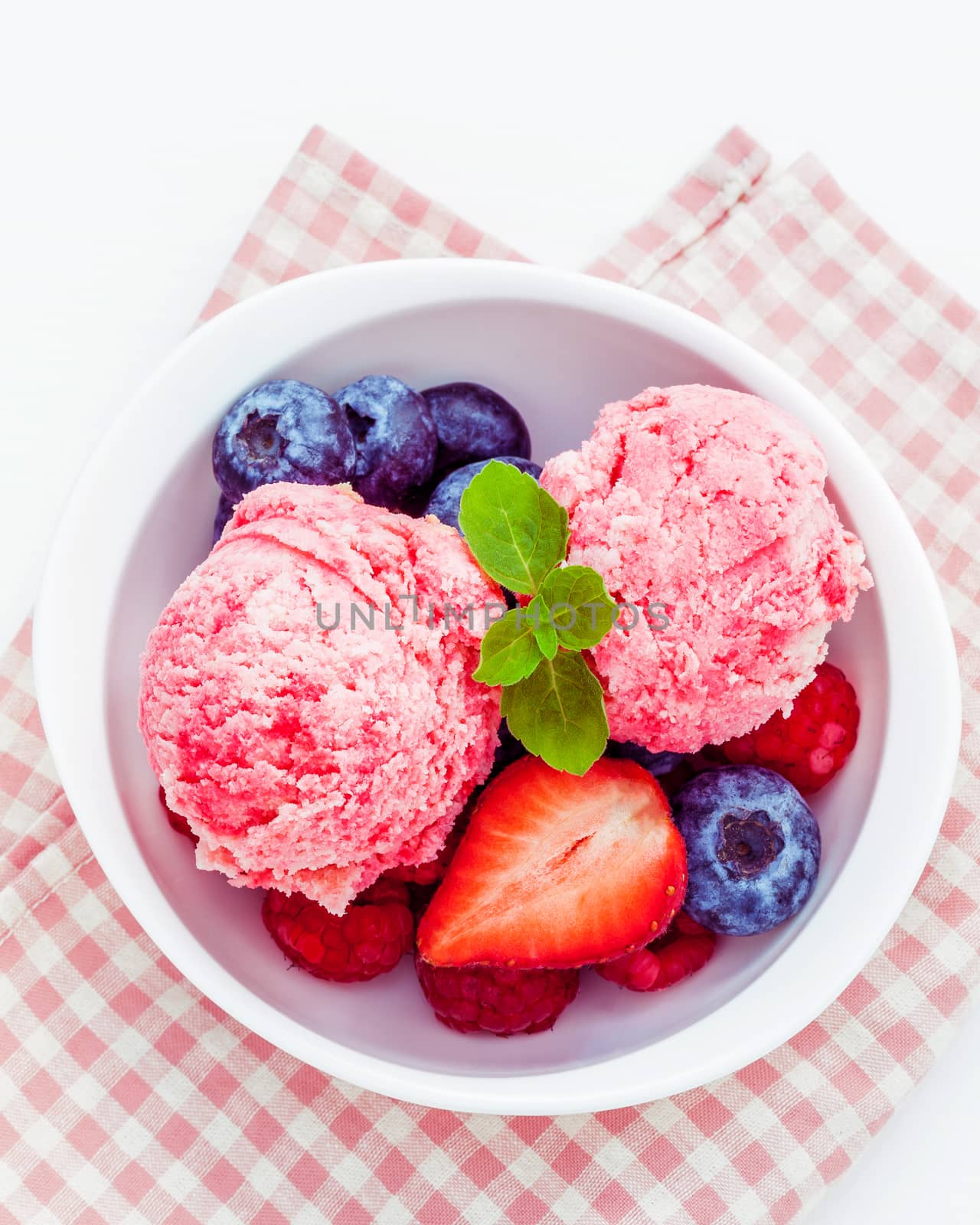 Close Up ice cream mixed berry fruits raspberry ,blueberry ,strawberry and peppermint leaves setup in white bowl on white wooden background . Summer and Sweet menu concept .