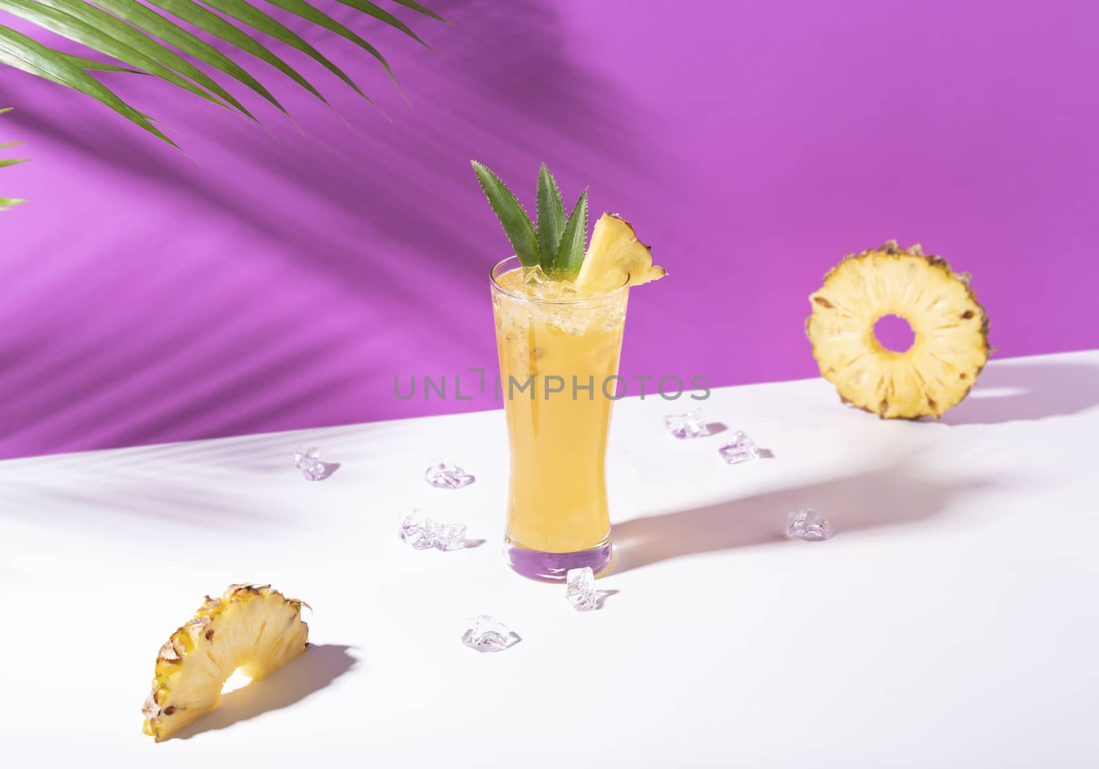 iced pineapple punch cocktail in glass on purple background. summer drink.