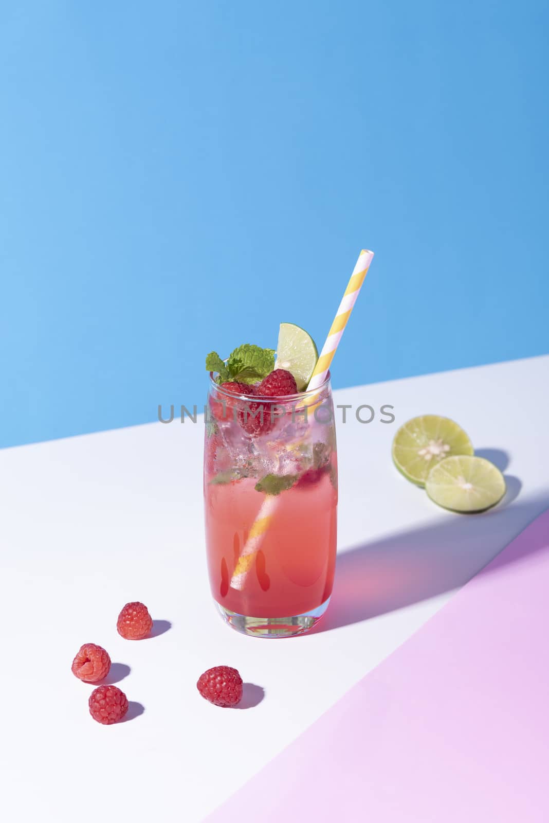 iced red raspberry punch cocktail with lime in glass on color background. summer drink.