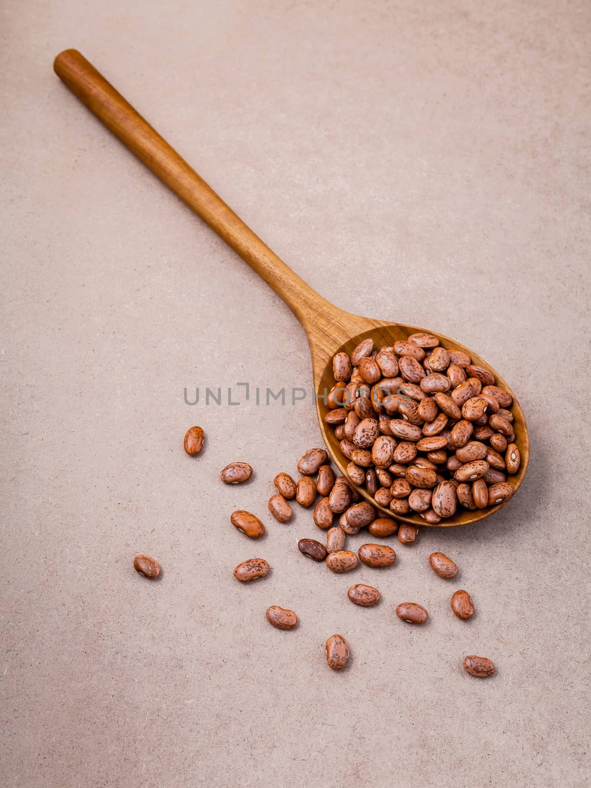 The composition of raw pinto beans in wooden spoon on brown back by kerdkanno