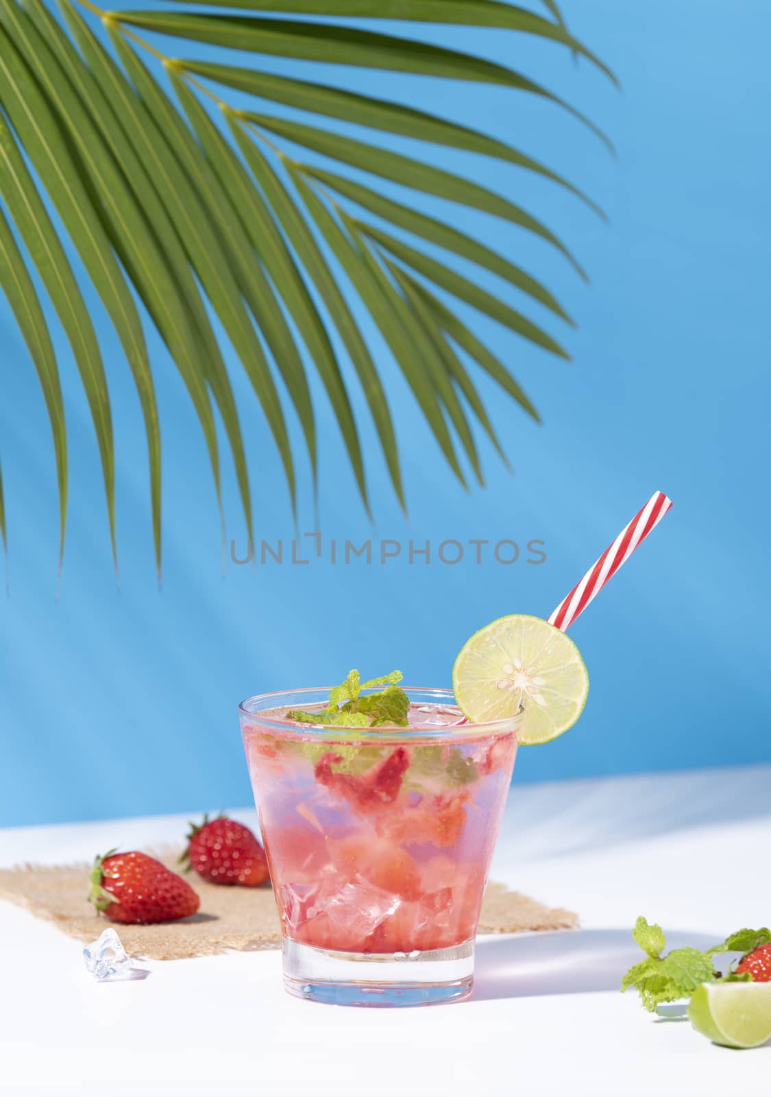 iced strawberry punch cocktail in glass with lemon on blue background. summer drink.