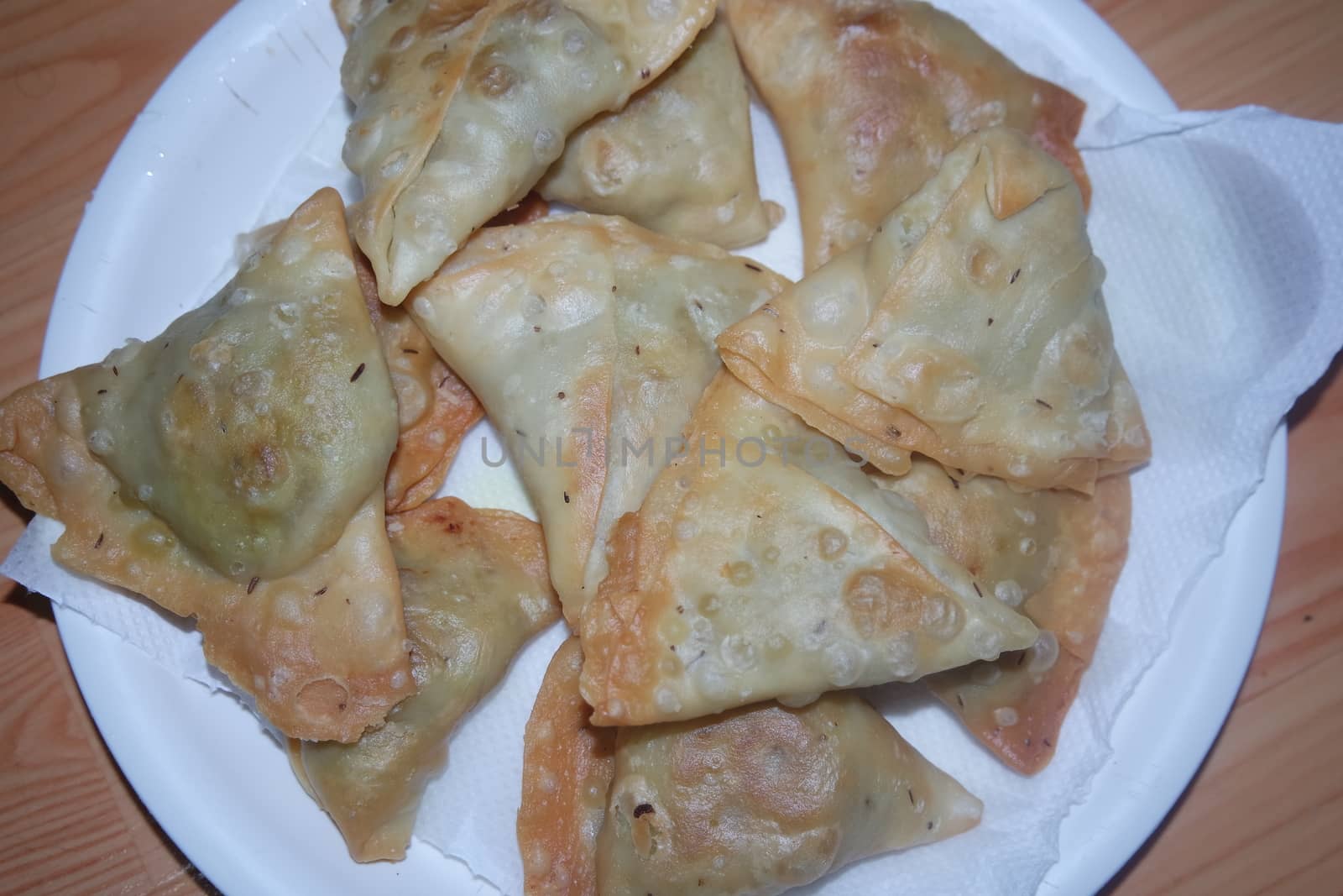 Closeup of delicious home made spicy and crunchy samosa pastries placed in a white ceramic plate on wooden floor