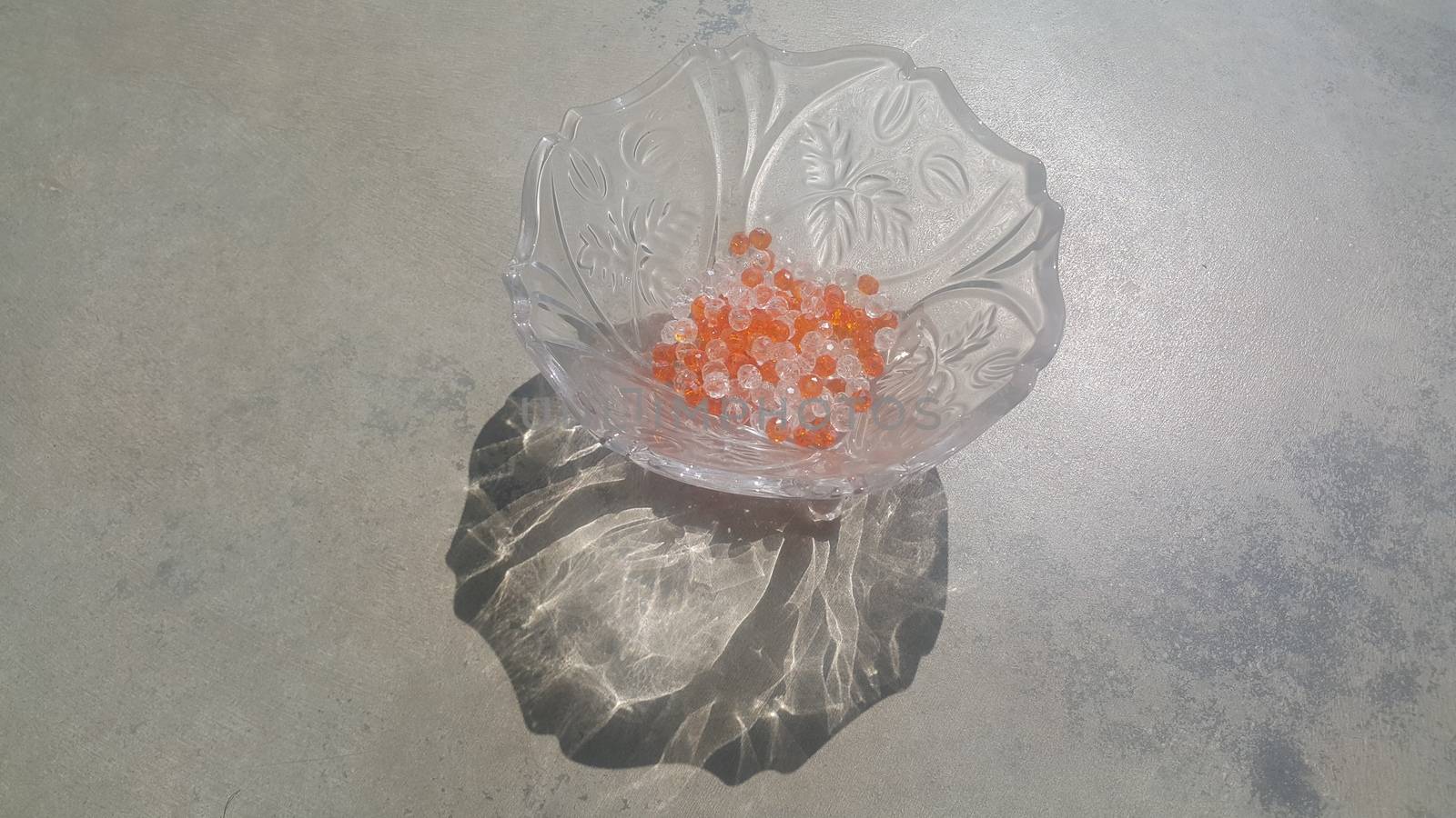 Shining, transparent, orange color crystal beads or gemstones or amber beads in a glass bowl over grey floor