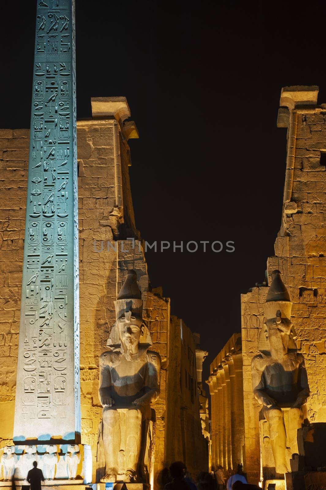 Large statue and obelisk at entrance pylon to ancient egyptian Luxor Temple lit up during night
